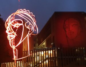 éclairage d'une sculpture d'un visage en fil d'acier avec ombre sur le bâtiment en arrière plan
