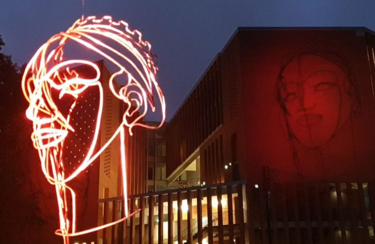 éclairage d'une sculpture d'un visage en fil d'acier avec ombre sur le bâtiment en arrière plan