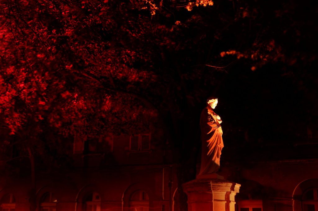 statue éclairée en rouge de face dans un jardin