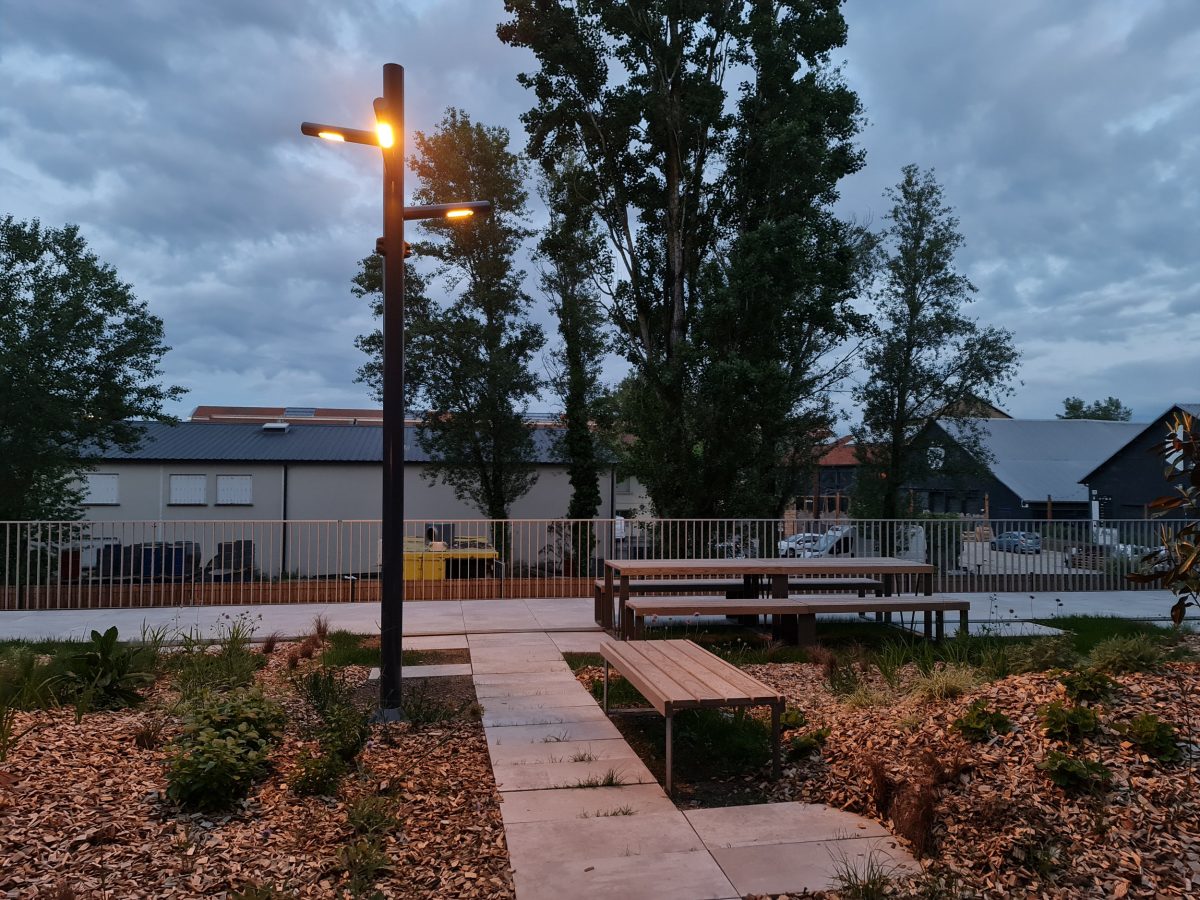 mât d'éclairage lumière chaude de technilum dans un parc avec des tables et des bancs